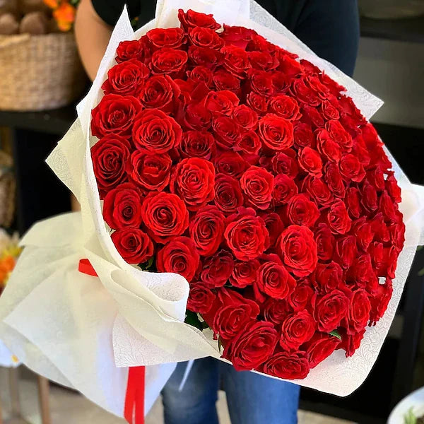 Bouquet of red roses wrapped in white paper held by a person.